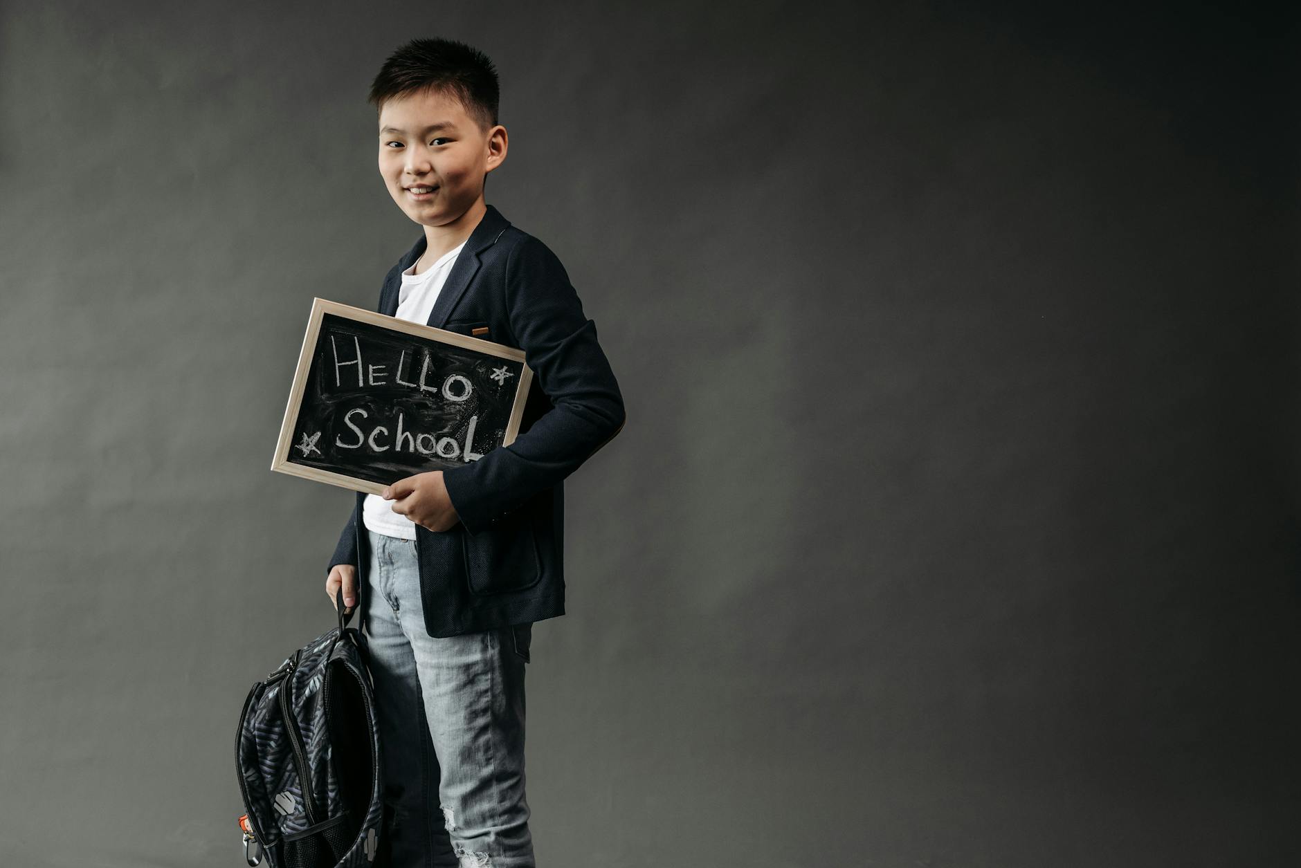Chłopiec z plecakiem trzymający tabliczkę z napisem Hello School