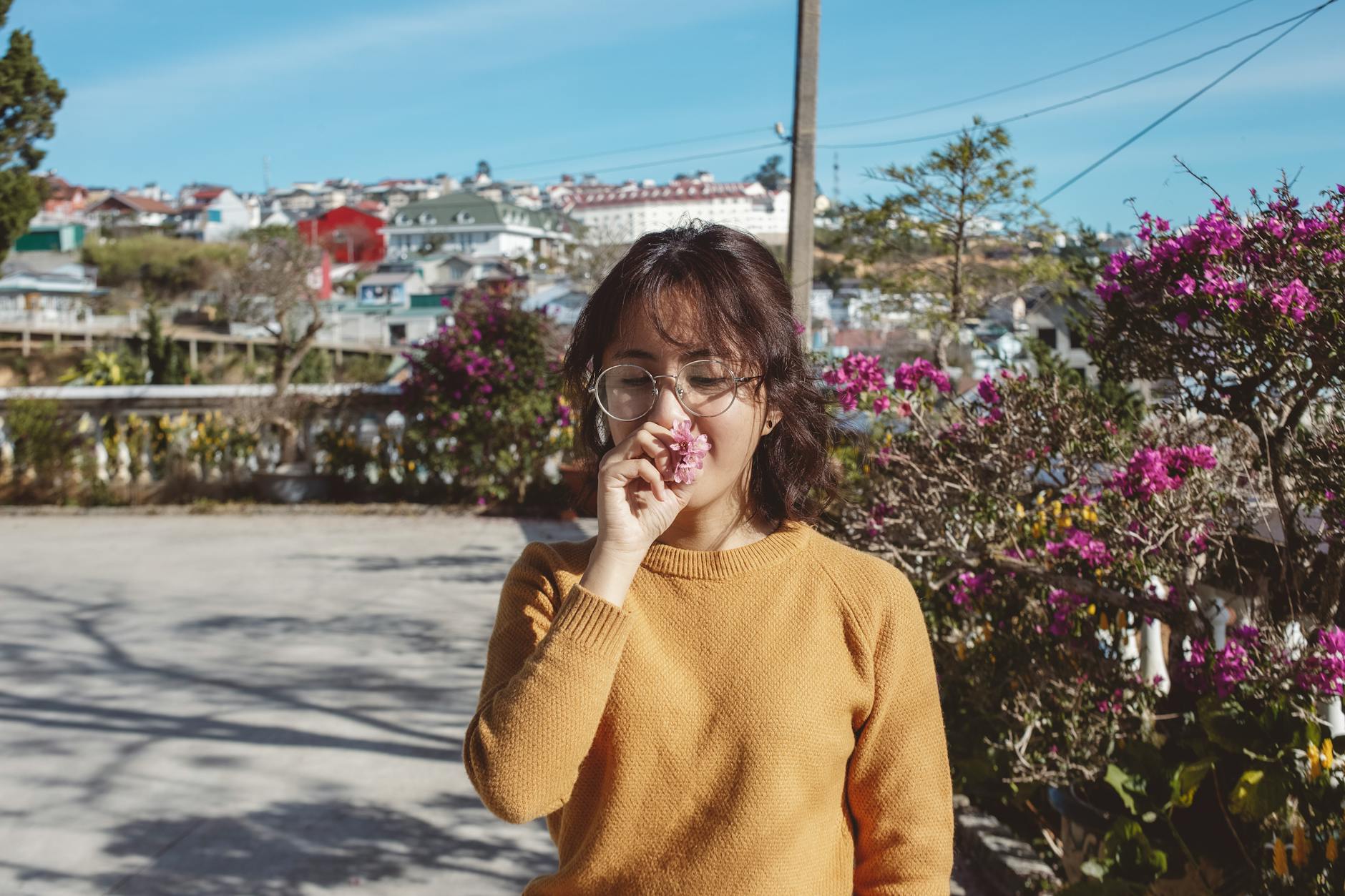 Uśmiechnięta Azjatka w okularach wącha różowe kwiaty na słonecznej ulicy