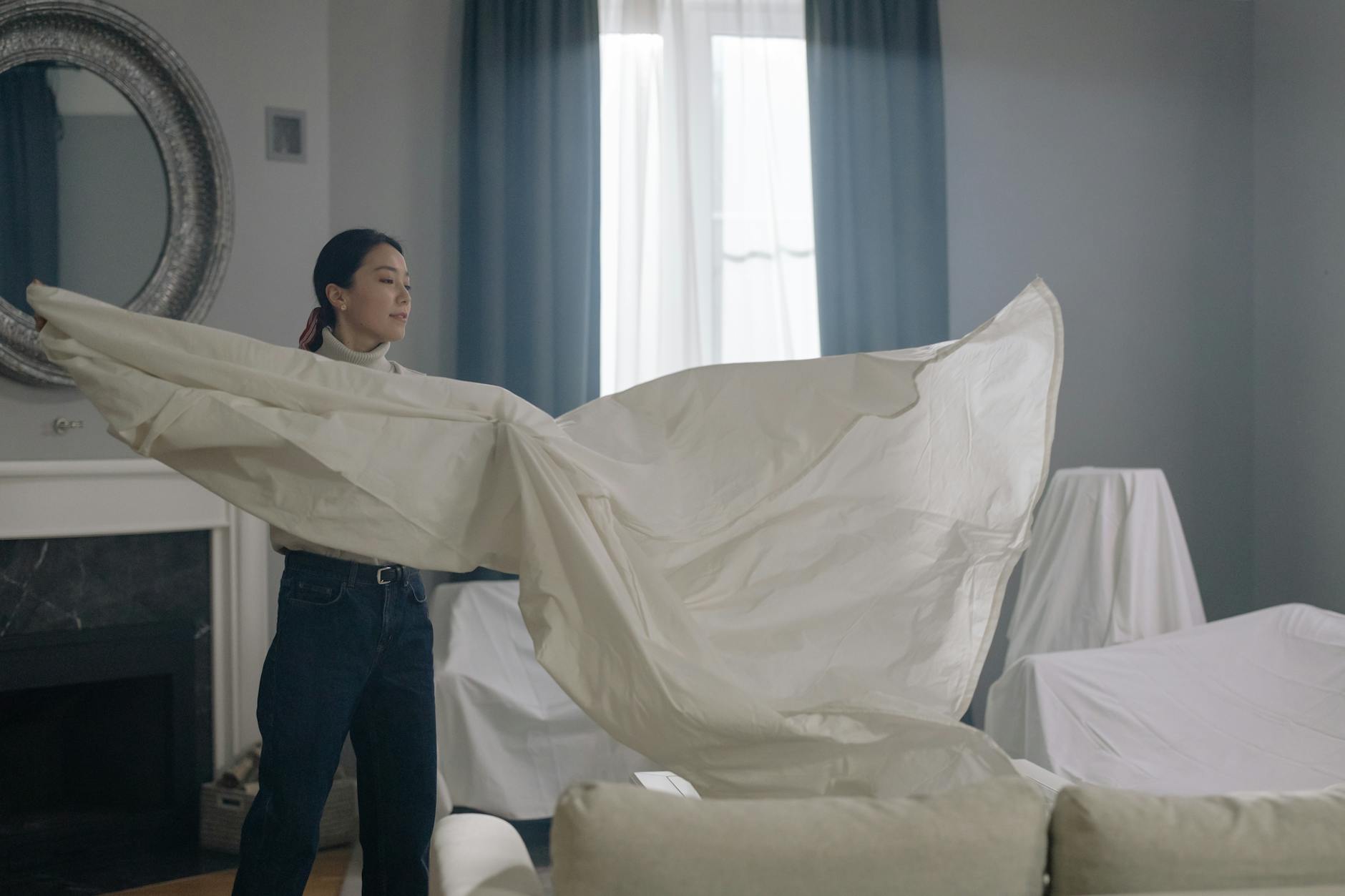 Kobieta w eleganckim salonie strzepuje dużą białą pościel