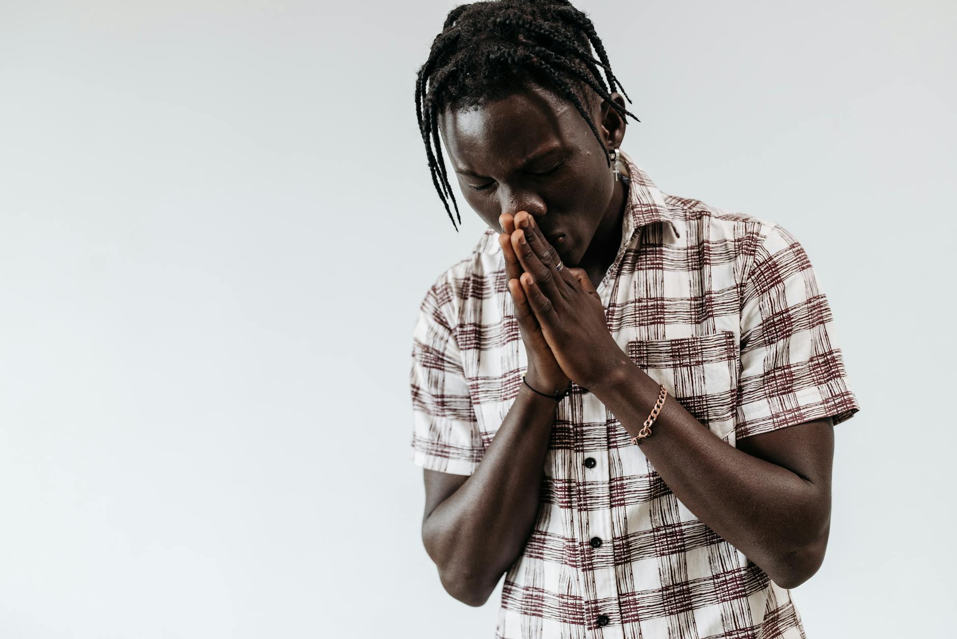 Młody mężczyzna w koszuli w kratę modli się z złożonymi dłońmi