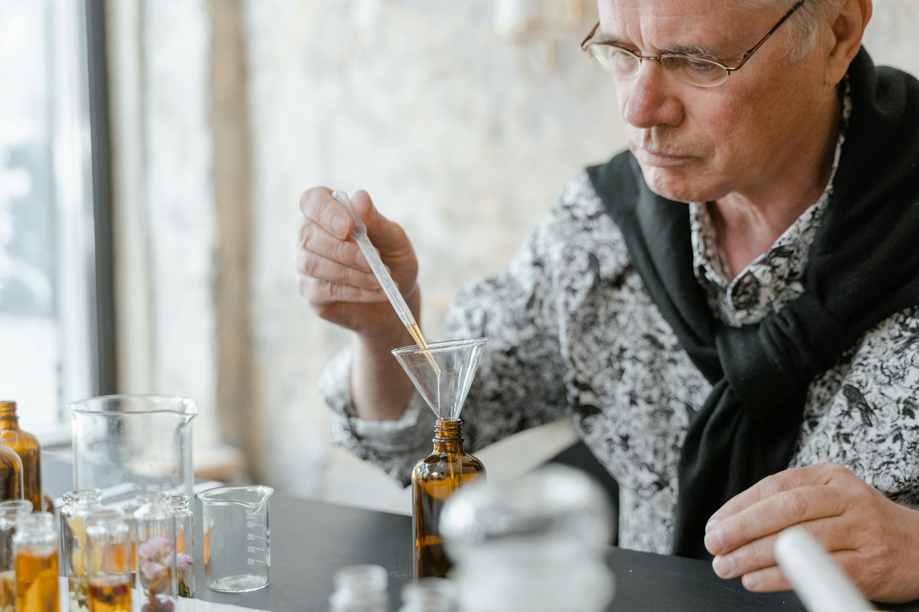 Starsza osoba odmierzająca pipetą olejki eteryczne do brązowych buteleczek